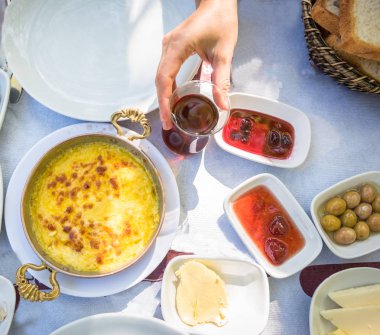 Bir piknik alanı dışında ahşap bir masaya üstten görünüm farklı gıda ile geleneksel Türk kahvaltı. İçecek çay bardağı tutan kadın el