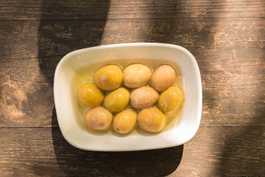 Arka plan doku eski ahşap masa ve bir tabak içinde büyük yeşil zeytin üstten görünüm 