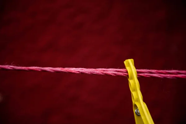 Vintage view of yellow Clothes peg pinned to a bench with red wall in a background hanging on a clothes rac