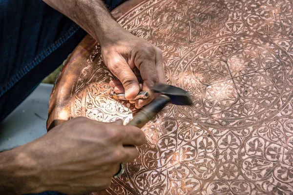 Senior craftsman,tinsmith,working with hammer during hand stamping or engraving decoration pattern on metal plate.Copper master, hands detail of craftsman at work.