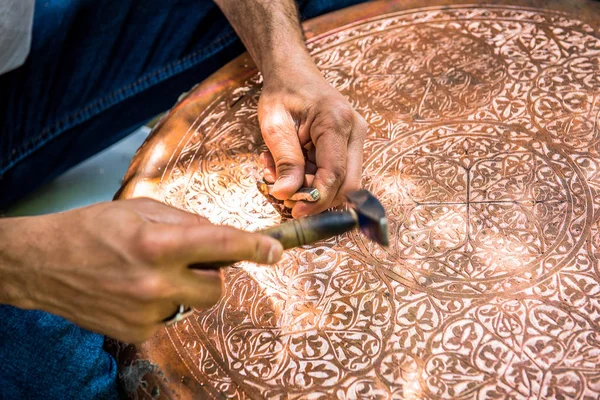 Senior craftsman,tinsmith,working with hammer during hand stamping or engraving decoration pattern on metal plate.Copper master, hands detail of craftsman at work.