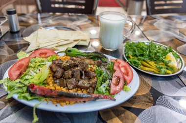 Türk şiş kebap dilimlenmiş lavaş, maydanoz, soğan, marul, domates, ızgara biber, Karışık turşu ve ayran ile beyaz bir tabakta servis ızgara lezzetli karaciğer ayrıntılı bir görünümünü kapat.