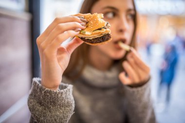 Güzel genç kız bir kafede fast food burger yiyor..