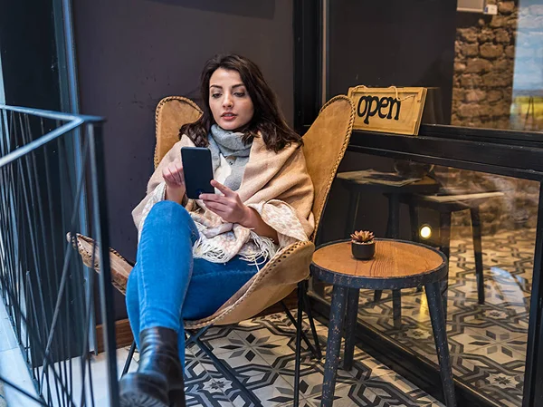 Moda kıyafetleri içinde güzel bir genç kız dışarıda bir kafede otururken akıllı telefonda kitap okur ya da mesajlaşır. Kadın yaşam tarzı konsepti.