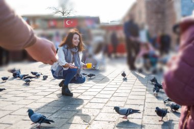 Bulanık görüntü: Moda kıyafetleri içindeki güzel kadın Eminonu, İstanbul ve Türkiye 'deki yeni cami meydanında güvercinleri besliyor
