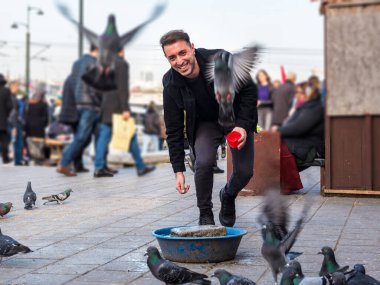 Bulanık görüntü: Moda kıyafetleri içindeki yakışıklı adam Eminonu, İstanbul ve Türkiye 'deki yeni cami meydanında güvercinleri besliyor
