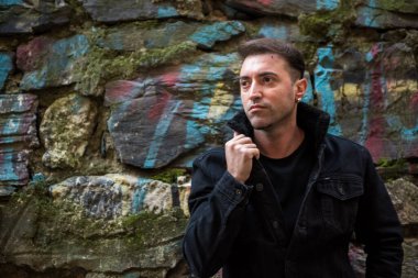 Küpeli yakışıklı, kendine güvenen olgun bir adam mesaj veya reklamınız için fotokopi alanı olan taştan yeşil, kahverengi arka planda duruyor..