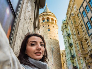 Şık giyinen güzel genç kız, Beyoğlu, İstanbul ve Türkiye 'deki tarihi Galata Kulesi manzaralı selfie çekiyor