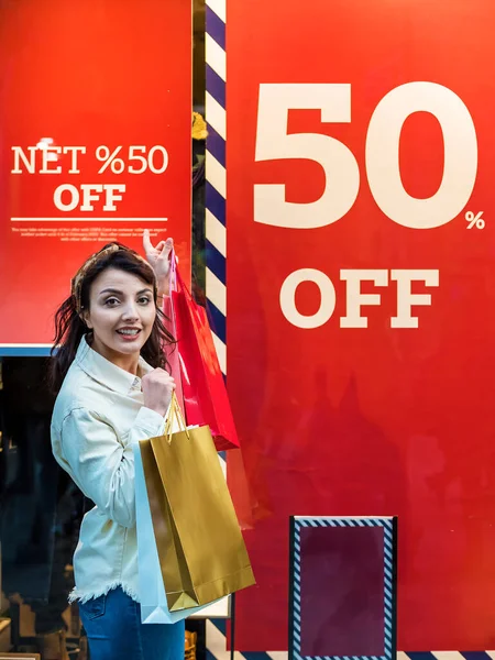 Beautiful woman in fashionable clothes shows listing sale on store showcases.Red sign on a shop window. Sale in a clothing store.Shopping, lifestyle concept