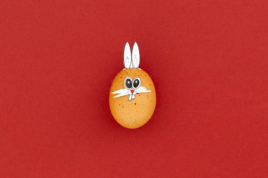 Kahverengi paskalya yumurtası, komik tavşan kulakları ve kırmızı arka planda çizgi film yüzü.