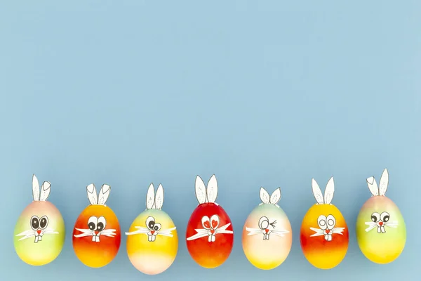 Colorful painted easter eggs with funny bunny ears and cartoon faces on light blue background