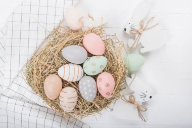 Paskalya sofrası, tatil masası dekorasyon fikri, beyaz tabaklar, çatal bıçak takımı, renkli pastel boya Paskalya yumurtaları, şenlikli dekor ve taze bahar çiçekleri ile düz konum.