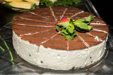 Yuvarlak dilimlenmiş pasta üzerinde çilek ve meyveler, cam bir tabakta basit bir masa. Tatlı tatlı için ev yapımı Fransız tarifi, nane yaprakları, kakao ve koyu çikolatalı kek.