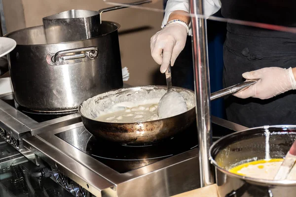 Chef preparing pasta during brunch buffet or food bloggers conference or catering event. Pasta station, hot food display, fresh pasta. Hands with gloves, pots and plates on stove, oven, live cooking