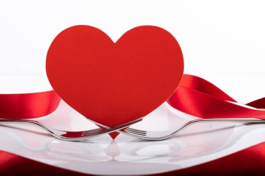 Çatal bıçaklı, çatallı, kırmızı saten kurdeleli, fotokopi alanı ve kalp şeklinde beyaz boş tabakla romantik bir akşam yemeği.