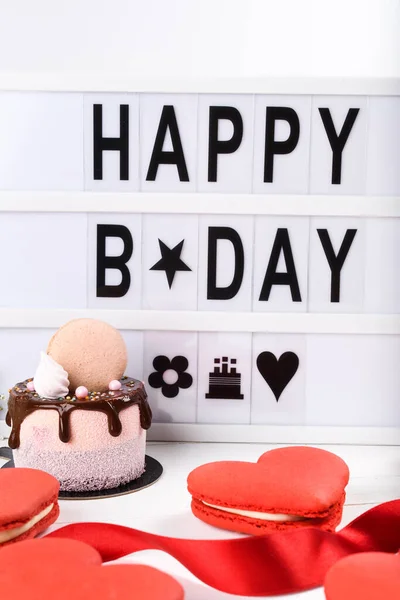 Happy Name Day light box wording plus mini cake dripping dessert. Spring Flowers and simple clean background. Macaroons red heart shaped