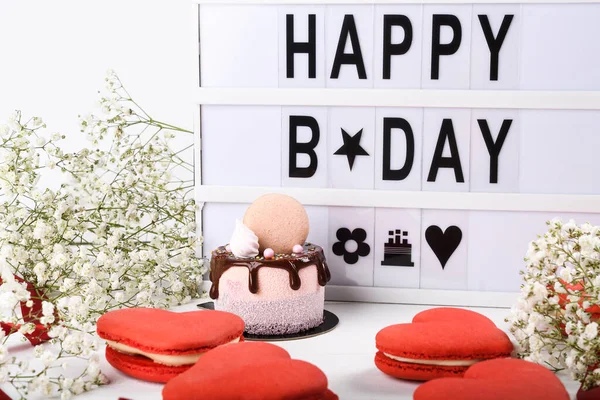 Happy Name Day light box wording plus mini cake dripping dessert. Spring Flowers and simple clean background. Macaroons red heart shaped