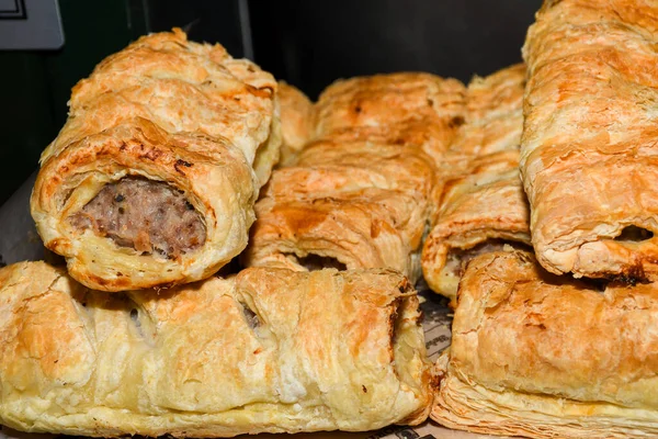 Traditional British puff pastry items, displayed in a bakery or pastry shop. Sausage rolls