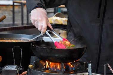 Profesyonel şef ve ateş. Arka planda açık ateşte sebze ve yemek pişirmek. Otel servisi fotoğrafı. Yatay görünüm.