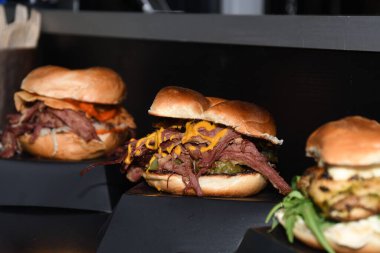 Fast food festivalinde yenmeye hazır taze erimiş hamburger. Açık hava yemek organizasyonu, brunch ya da fast food ile akşam yemeği partisi. Erimiş peynir ve altın çörek. İştah açıcı ev yapımı hamburger.