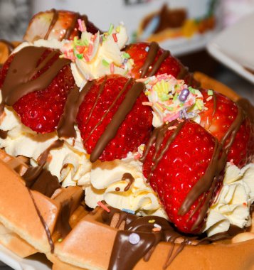 Beyaz ve koyu çikolata soslu gözlemeler, çilek ve muz gibi meyveler.