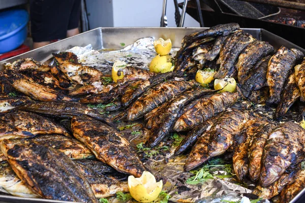 Freshly grilled fish on counter top stall, during seafood festival, street food market. Red sea bass, trout, sword fish, fried golden calamari, diverse seafood variety selection closeup, top view.