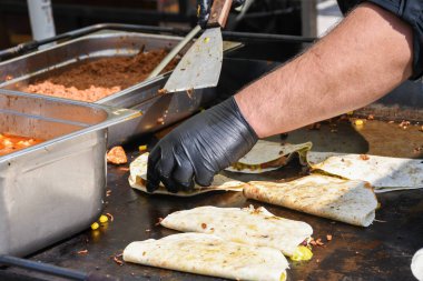 Quesadilla hazırlama süreci, geleneksel Meksika yemeği. Açık hava ortamları, yemek festivali sırasında aşçı yemekleri, otantik sokak yemekleri. Siyah eldivenler lezzetli malzemeler. Aşçı pidenin üstünde takla atar.
