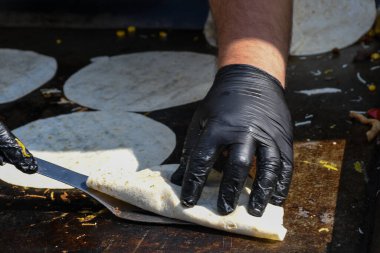 Quesadilla hazırlama süreci, geleneksel Meksika yemeği. Açık hava ortamları, yemek festivali sırasında aşçı yemekleri, otantik sokak yemekleri. Siyah eldivenler lezzetli malzemeler. Aşçı pidenin üstünde takla atar.