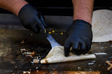 Quesadilla hazırlama süreci, geleneksel Meksika yemeği. Açık hava ortamları, yemek festivali sırasında aşçı yemekleri, otantik sokak yemekleri. Siyah eldivenler lezzetli malzemeler. Aşçı pidenin üstünde takla atar.