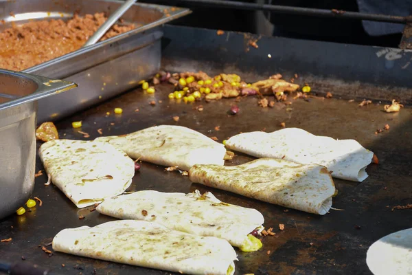The process of preparing a quesadilla, traditional Mexican dish. Outdoor outside setting, chef cooking during food festival, authentic street food. Black gloves tasty ingredients. Cook flips over pita