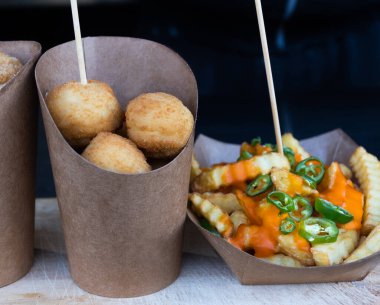 Kahverengi bir kağıt koni içinde Sicilya arancini grubu ve peynir kremalı patates kızartması ve doğrudan güneş ışığı altında bir sokak yemeği pazarında doğranmış jalapanelos, seçici bir odak noktası. Geleneksel otantik