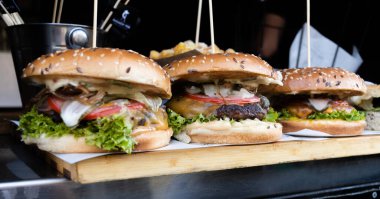 Fast food festivalinde yenmeye hazır taze erimiş hamburger. Açık hava yemek organizasyonu, brunch ya da fast food ile akşam yemeği partisi. Erimiş peynir ve altın çörek. İştah açıcı ev yapımı hamburger.