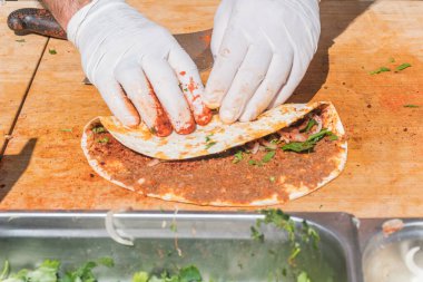 Lahmacun adı verilen geleneksel Türk pizzası, et, soğan ve maydanozla bir sokak yiyecek pazarında ahşap bir masada sergileniyor.