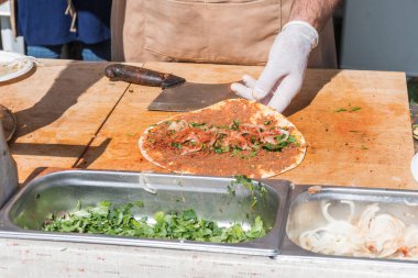 Lahmacun adı verilen geleneksel Türk pizzası, et, soğan ve maydanozla bir sokak yiyecek pazarında ahşap bir masada sergileniyor.