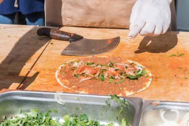 Lahmacun adı verilen geleneksel Türk pizzası, et, soğan ve maydanozla bir sokak yiyecek pazarında ahşap bir masada sergileniyor.