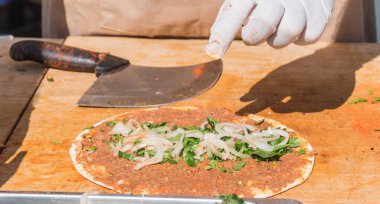 Lahmacun adı verilen geleneksel Türk pizzası, et, soğan ve maydanozla bir sokak yiyecek pazarında ahşap bir masada sergileniyor.