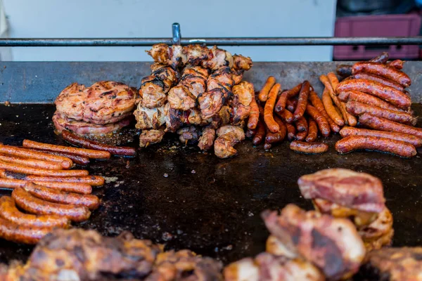 Chef preparing meat on the grill, during outdoor outside food festival, food truck, brunch or catering event. Pork steaks, chicken breast, sausages, high protein unhealthy or fat pieces of meat chops