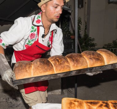Bükreş, Romanya, 1 Eylül 2019: Geleneksel kıyafet giymiş bir adam ekmek hazırlıyor. Ahşap taş fırınında taze pişmiş ekmek.
