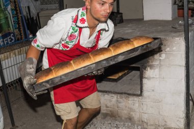 Bükreş, Romanya, 1 Eylül 2019: Geleneksel kıyafet giymiş bir adam ekmek hazırlıyor. Ahşap taş fırınında taze pişmiş ekmek.