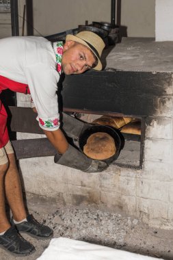 Bükreş, Romanya, 1 Eylül 2019: Geleneksel kıyafet giymiş bir adam ekmek hazırlıyor. Ahşap taş fırınında taze pişmiş ekmek.