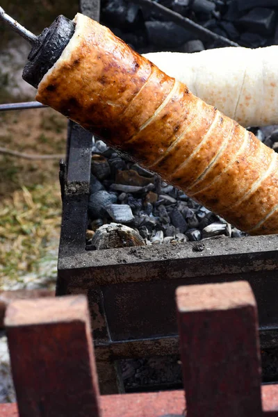 Kurtos kalacs or chimney cakes, preparing cooking on charcoal grill, street food traditional Hungarian, during food festival. Kurtos Kalacs traditional hungarian cake, baked with sugar, honey and nuts