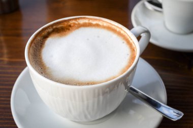 Süt köpüklü sade kahve fincanı beyaz seramik tabakta, ahşap arka planda. Kopya alanı ile izole edilmiş. Kahvaltı konsepti otel espresso ya da kapuçino içeceği.