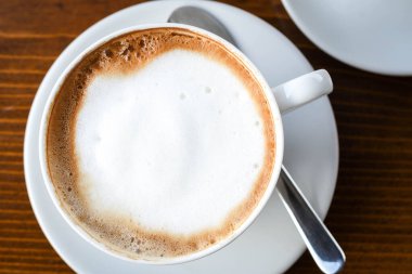 Süt köpüklü sade kahve fincanı beyaz seramik tabakta, ahşap arka planda. Kopya alanı ile izole edilmiş. Kahvaltı konsepti otel espresso ya da kapuçino içeceği.