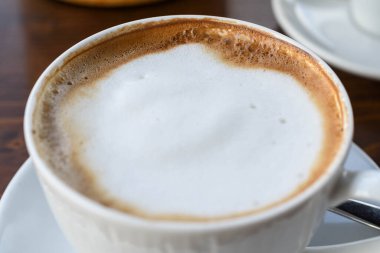 Süt köpüklü sade kahve fincanı beyaz seramik tabakta, ahşap arka planda. Kopya alanı ile izole edilmiş. Kahvaltı konsepti otel espresso ya da kapuçino içeceği.
