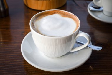 Süt köpüklü sade kahve fincanı beyaz seramik tabakta, ahşap arka planda. Kopya alanı ile izole edilmiş. Kahvaltı konsepti otel espresso ya da kapuçino içeceği.