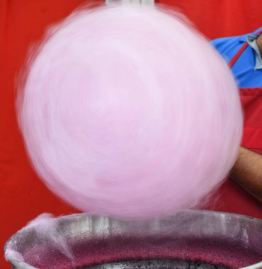 Hand rolling cotton candy in candy floss machine. Making candyfloss during street food festival. Treat for children at country fair. Pink or purple sweetened cotton candy on stick for sale clipart