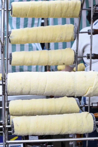 Kurtos kalacs or chimney cakes, preparing cooking on charcoal grill, street food traditional Hungarian, during food festival. Kurtos Kalacs traditional hungarian cake, baked with sugar, honey and nuts