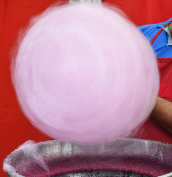 Hand rolling cotton candy in candy floss machine. Making candyfloss during street food festival. Treat for children at country fair. Pink or purple sweetened cotton candy on stick for sale