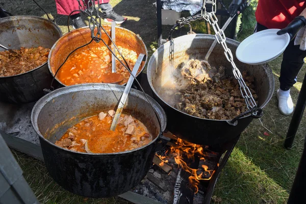 Very large cauldron cooking food during campfire, big pots on fire preparing during food festival. Tourist pot hanging over the fire on a tripod. Cooking in a pot on the fire. Camping concept