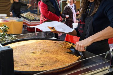 Nice, France, 25th of February 2020: big Plate of Farinata or Cecina or Torta di ceci thin unleavened pancake or crepe of chickpea flour originating in Genoa cooked in a wood oven, socca for sale clipart